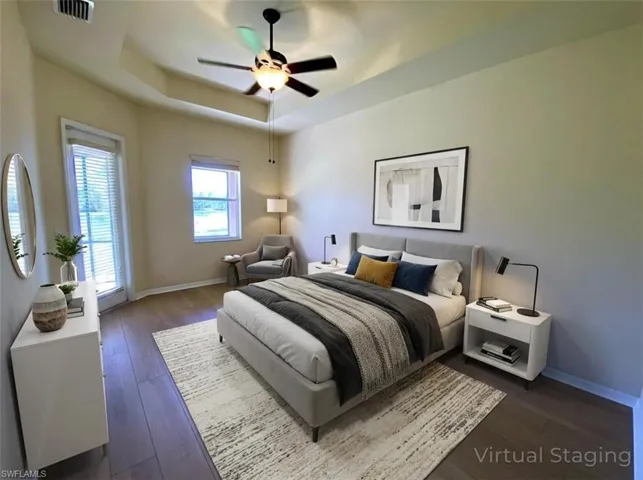 Bedroom with a raised ceiling, dark wood finished floors, and a ceiling fan