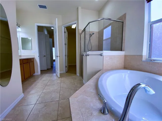 Bathroom featuring a spacious closet, a bath, vanity, a shower stall, and light tile patterned floors