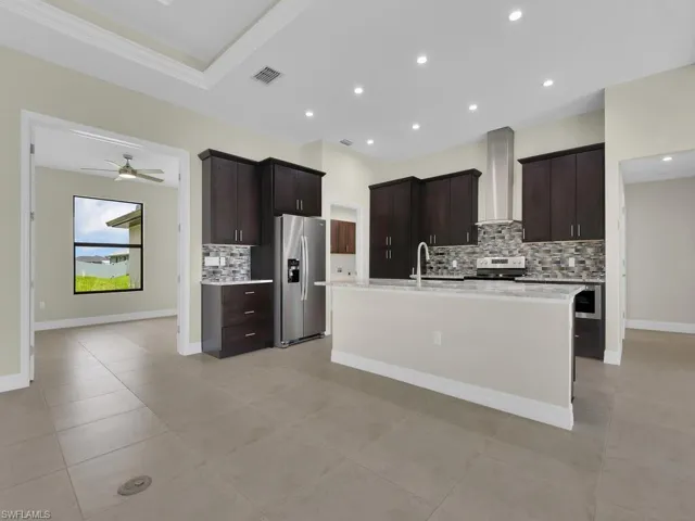Kitchen featuring decorative backsplash, dark brown cabinets, stainless steel appliances, ceiling fan, and wall chimney range hood