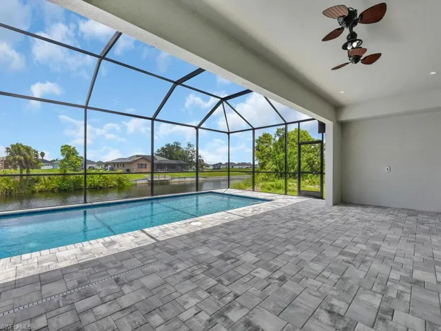 View of pool with glass enclosure, ceiling fan, a patio area, and a water view