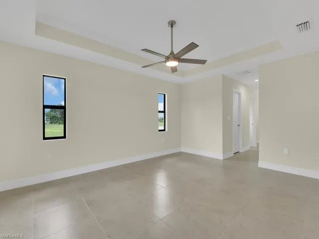 Tiled empty room with a tray ceiling, a wealth of natural light, and ceiling fan