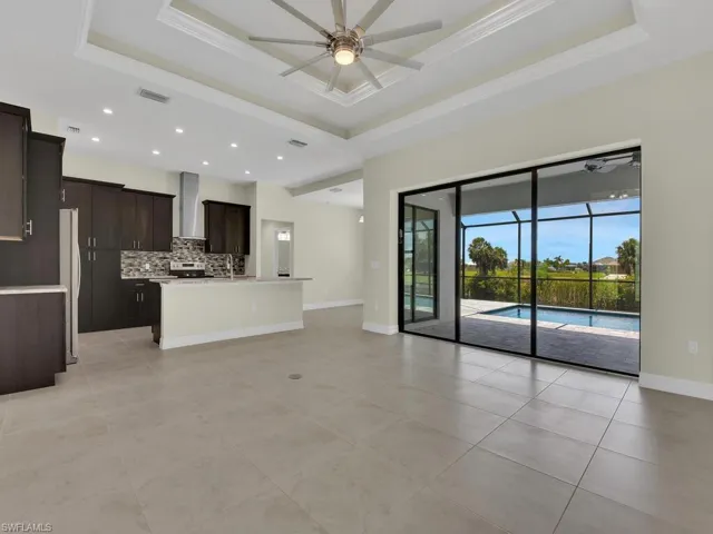 Kitchen with ceiling fan, wall chimney range hood, a raised ceiling, tasteful backsplash, and a center island with sink