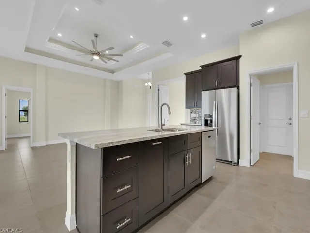 Kitchen with a raised ceiling, stainless steel appliances, sink, and an island with sink