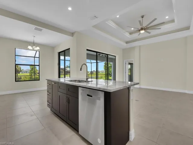 Kitchen featuring light stone counters, ceiling fan with notable chandelier, sink, a center island with sink, and dishwasher