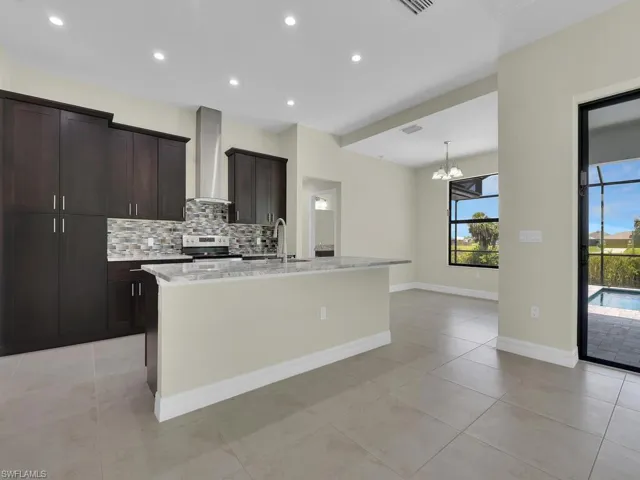 Kitchen with backsplash, a center island with sink, stainless steel electric stove, and wall chimney range hood