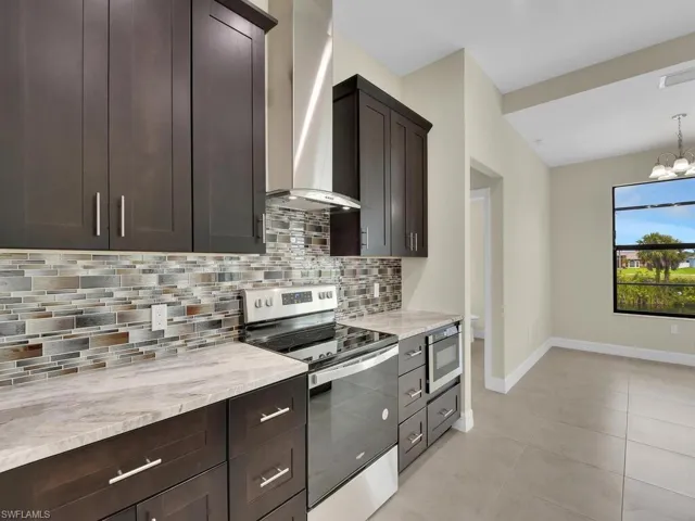 Kitchen featuring wall chimney exhaust hood, dark brown cabinets, backsplash, and appliances with stainless steel finishes