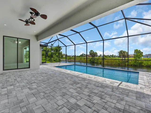 View of swimming pool featuring ceiling fan, a water view, a patio, and glass enclosure