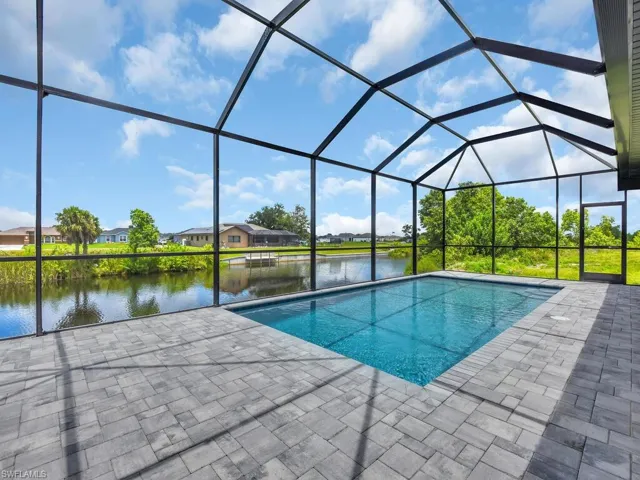 View of swimming pool featuring glass enclosure, a water view, and a patio