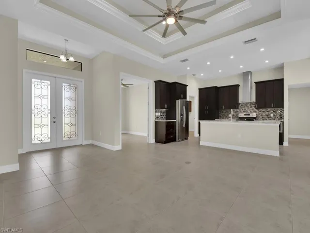 Unfurnished living room featuring ceiling fan with notable chandelier, a raised ceiling, crown molding, and french doors