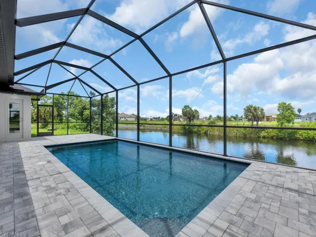 View of pool with glass enclosure, a patio area, and a water view