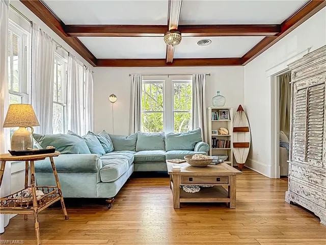 Living area with baseboards, visible vents, light wood-style floors, and beam ceiling