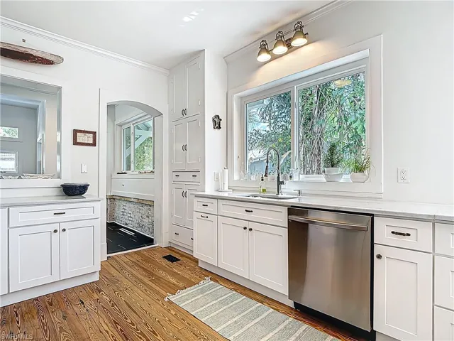Kitchen featuring ornamental molding, a sink, arched walkways, dishwasher, and wood finished floors