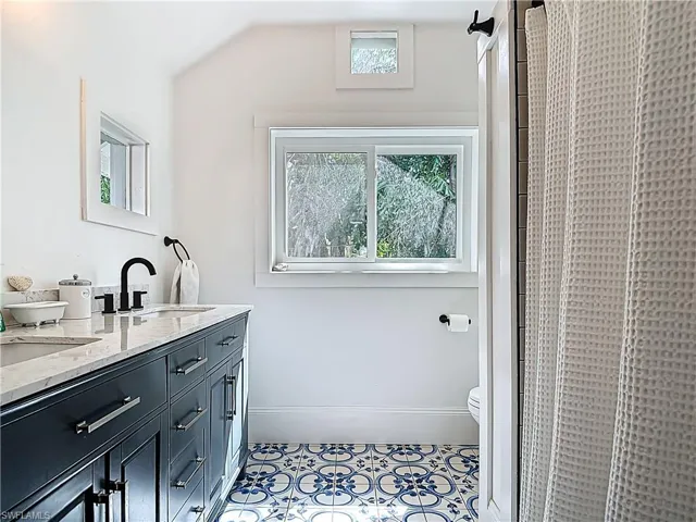 Bathroom with tile patterned floors, toilet, a sink, a shower with curtain, and double vanity