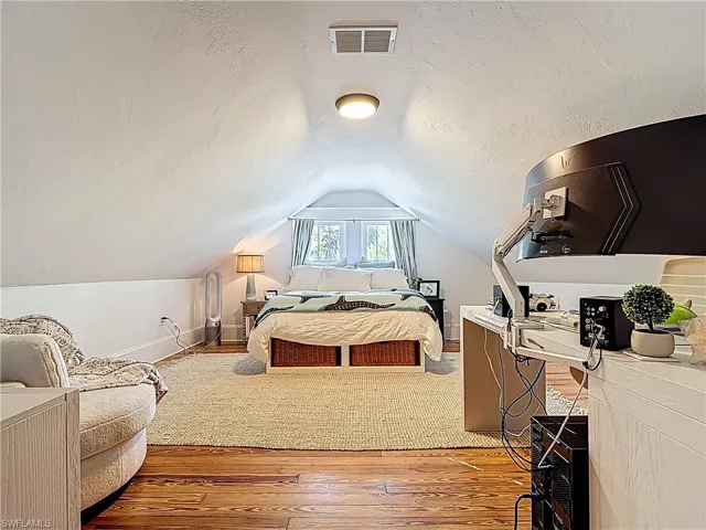 Bedroom with a textured ceiling, visible vents, light wood finished floors, baseboards, and vaulted ceiling