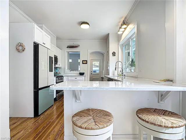 Kitchen featuring dark wood-style flooring, white cabinets, a breakfast bar, appliances with stainless steel finishes, and a sink