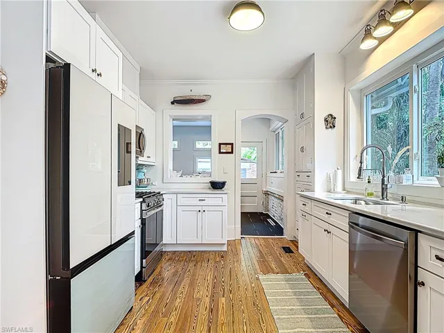 Kitchen featuring light countertops, wood finished floors, stainless steel appliances, arched walkways, and a sink
