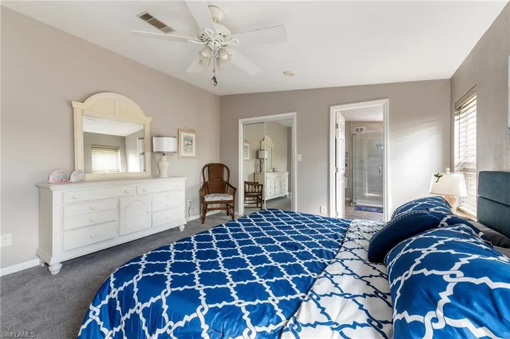 Carpeted bedroom with ceiling fan, ensuite bath, and lofted ceiling