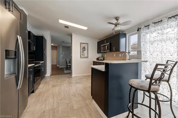 Kitchen with stainless steel appliances, ornamental molding, a breakfast bar, dark cabinets, and a ceiling fan