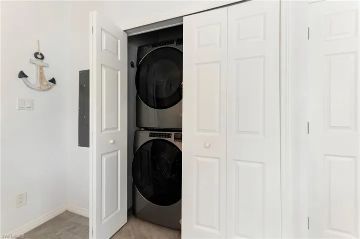 Washroom with stacked washing machine and dryer, electric panel, and light tile patterned floors