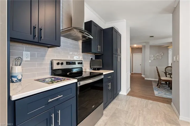 Kitchen with stainless steel electric stove, wall chimney range hood, ornamental molding, and decorative backsplash