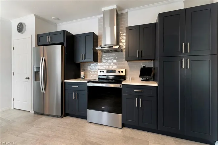 Kitchen featuring appliances with stainless steel finishes, wall chimney range hood, crown molding, tasteful backsplash, and light stone countertops