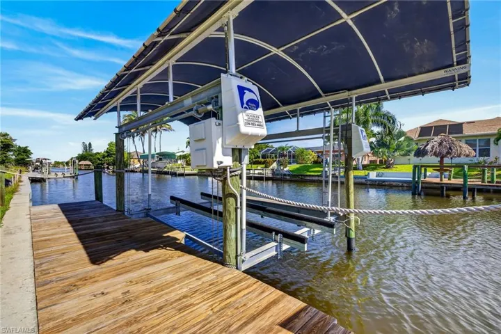 Waterfront dock with a covered boat lift, featuring a wood-plank deck, canal access, and a clear blue sky overhead