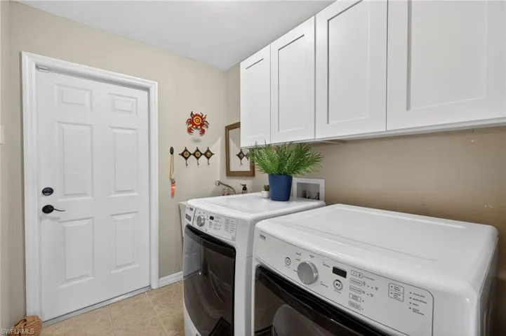 Functional laundry area featuring upper white shaker-style cabinetry, a white paneled door with black hardware, and neutral-toned wall paint