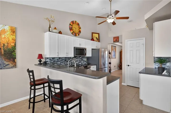 Kitchen featuring a breakfast bar with stone countertops, white shaker-style cabinetry, and a patterned tile backsplash