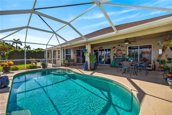 Screened lanai featuring a freeform swimming pool with integrated steps, an expansive concrete patio, and mature landscaping