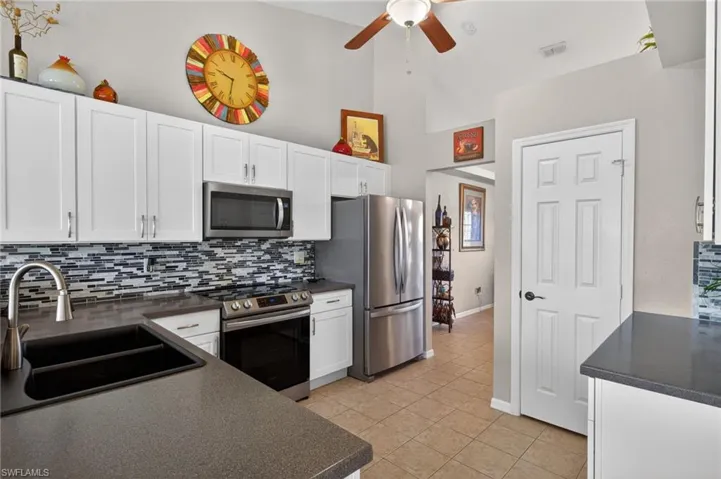 Kitchen featuring white shaker-style cabinetry, dark countertops, and a mosaic tile backsplash
