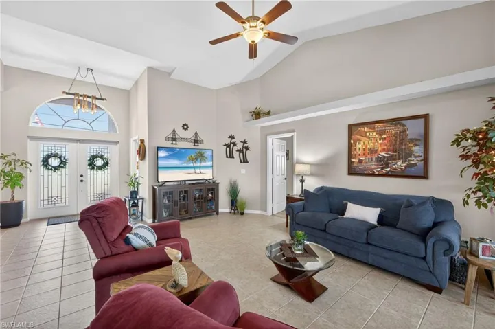 Living area featuring vaulted ceilings with a ceiling fan, tile flooring, and double entry doors with an arched transom window