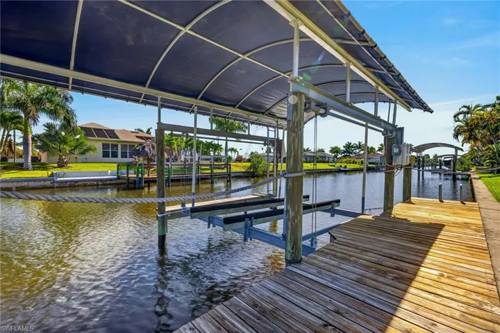 Waterfront dock featuring a covered boat lift, wood-plank decking, and a rope barrier