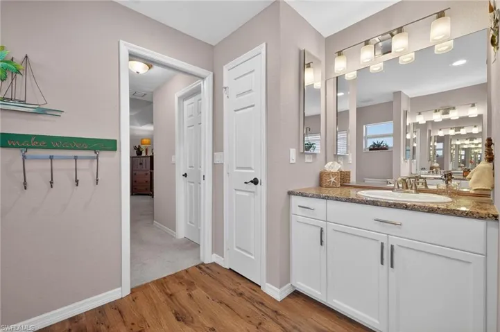 Bathroom vanity featuring a single basin, granite-style countertop, white cabinetry with brushed nickel hardware, and an expansive mirror with a multi-bulb light fixture