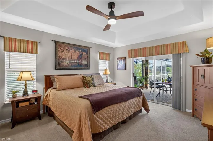 Spacious room featuring tray ceilings with a ceiling fan, carpet flooring, and direct access to an enclosed patio through sliding glass doors