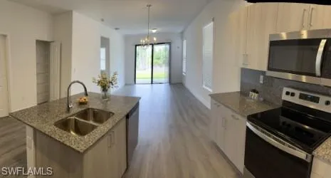 Kitchen with appliances with stainless steel finishes, dark stone countertops, light wood-style floors, and a chandelier