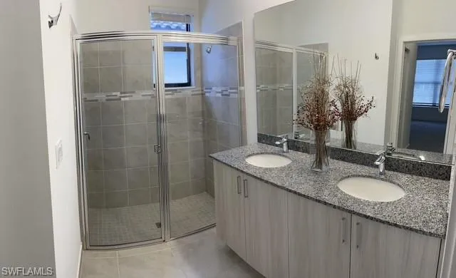 Full bathroom featuring double vanity, a shower stall, and light tile patterned flooring