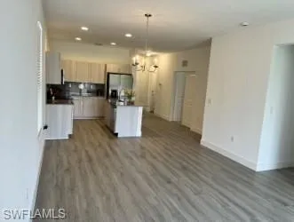 Kitchen featuring dark countertops, a chandelier, open floor plan, light brown cabinetry, and decorative light fixtures