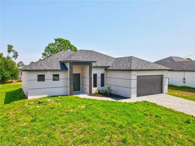 View of front facade featuring a front lawn, roof with shingles, stucco siding, and decorative driveway