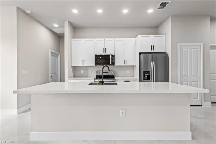 Kitchen featuring stainless steel appliances, a center island with sink, white cabinetry, light stone counters, and recessed lighting