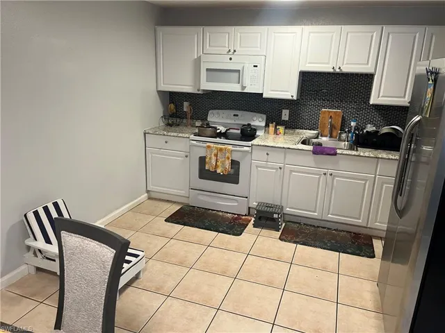 Kitchen with white appliances, light tile patterned flooring, white cabinetry, tasteful backsplash, and light stone countertops
