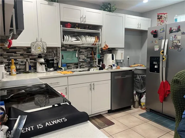 Kitchen featuring white cabinets, appliances with stainless steel finishes, light tile patterned flooring, light stone countertops, and tasteful backsplash