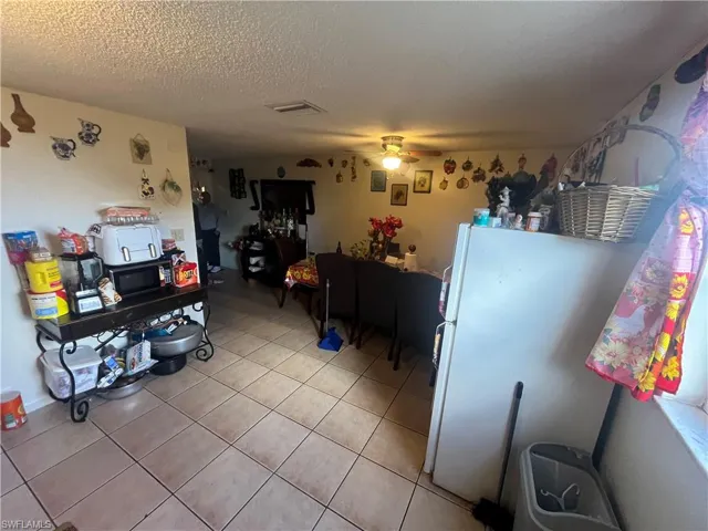 Kitchen with freestanding refrigerator, a textured ceiling, ceiling fan, black microwave, and light tile patterned floors