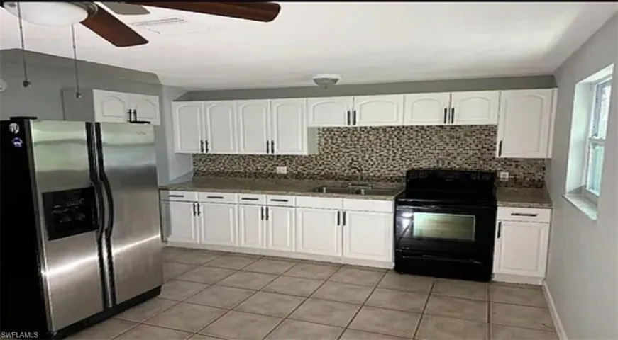 Kitchen with stainless steel fridge with ice dispenser, black / electric stove, white cabinets, ceiling fan, and decorative backsplash