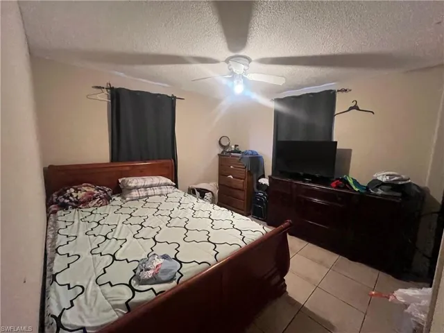 Bedroom with ceiling fan, light tile patterned floors, and a textured ceiling