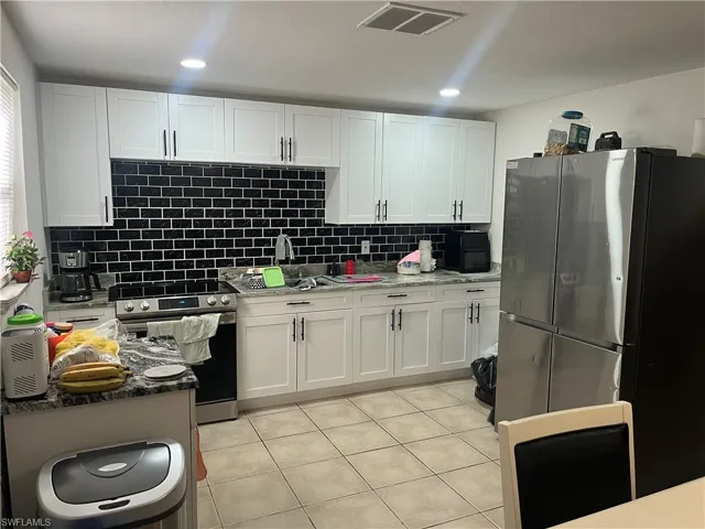 Kitchen featuring stainless steel appliances, dark stone countertops, white cabinets, and light tile patterned floors