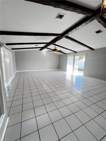Empty room with light tile patterned flooring, vaulted ceiling with beams, and a ceiling fan