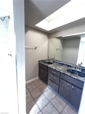 Full bath with double vanity, light tile patterned floors, and a skylight