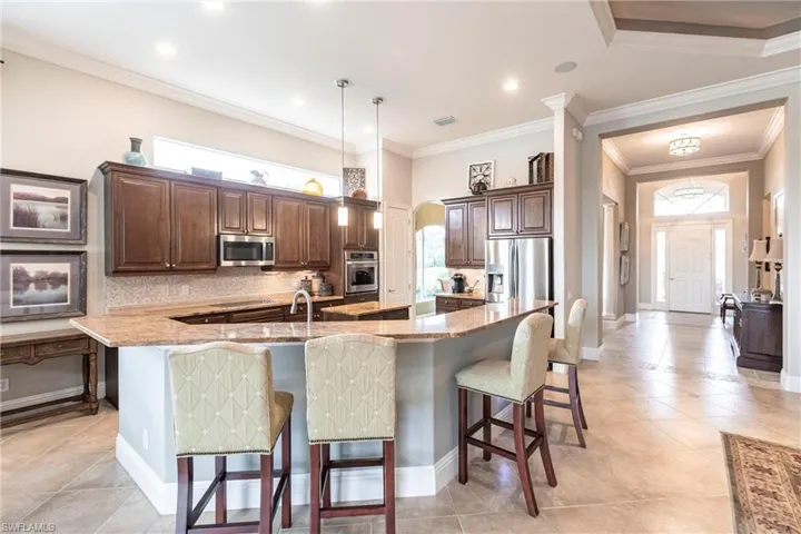 Kitchen featuring dark brown cabinetry, arched walkways, a kitchen bar, light tile patterned floors, and ornamental molding