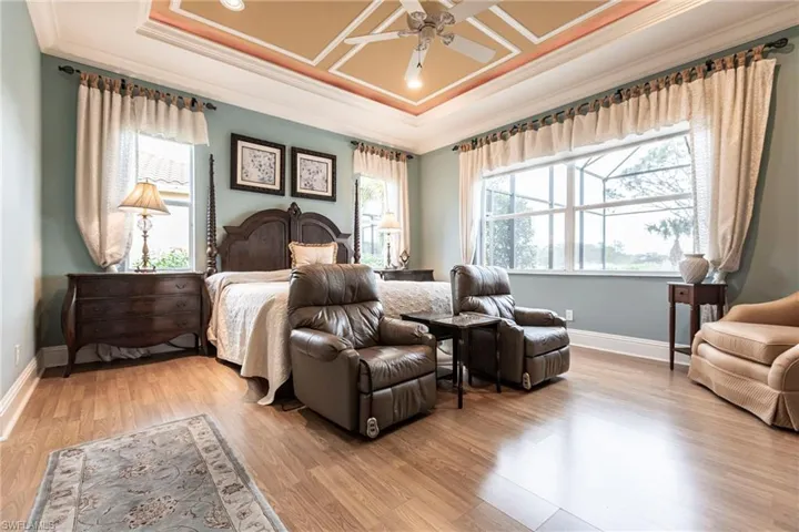 Bedroom featuring ornamental molding, a tray ceiling, light wood finished floors, and ceiling fan