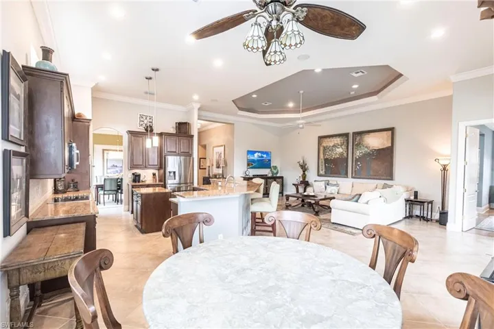Dining space featuring crown molding, arched walkways, a ceiling fan, a tray ceiling, and light tile patterned floors